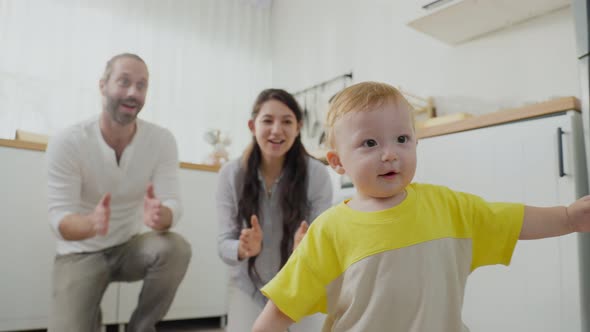 Caucasian baby boy child learn to walk with parents support and helping son to walk in house. alt