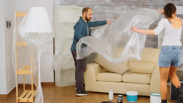 Couple Wrapping Sofa in Plastic Foil