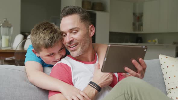 Happy caucasian father with son sitting in living room and using tablet