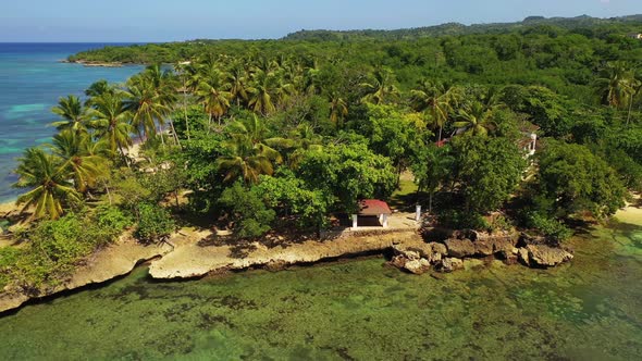 Tropical travel destination with green lush palm trees on rocky coastline with clear shallow water,