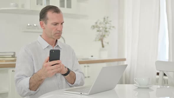 Professional Middle Aged Man Using Smartphone and Laptop at Home