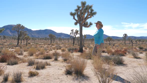 Woman Walking In Dry Desert With Huge Rocks Hills And Joshua Tree Cactus