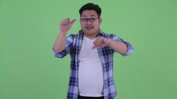 Confused Young Overweight Asian Hipster Man Choosing Between Thumbs Up and Thumbs Down