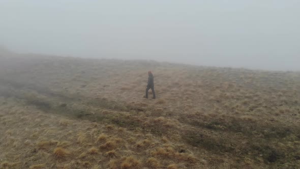 A Caucasian Man in Tourist Clothing Walks on the Top of a Plateau Next to a Deep Cliff Along with a