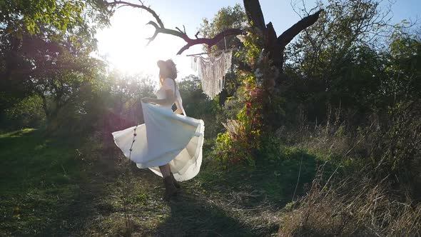 A young beautiful brunette in a white dress rotates and waves her dress on a meadow in the forest. S