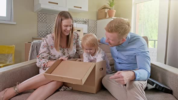 Parents and Two Little Daughters Sit on Floor and Unpack Family Suitcase in New House