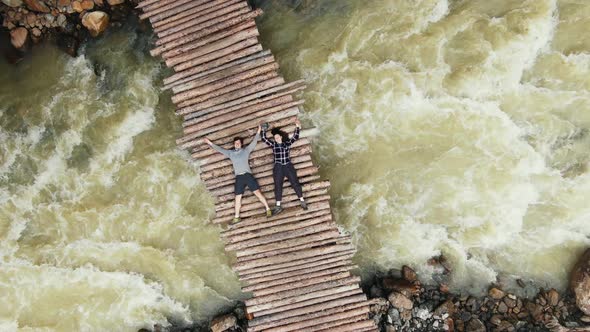 Man and Woman Lie on Wooden Footbridge Over Rough River