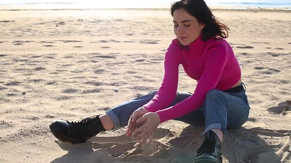 Young Woman Playing with Sand on the Beach on the Sea Background