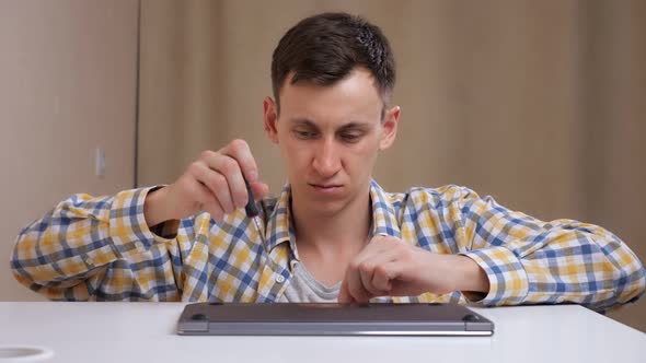 Man Disassembles Laptop with Screwdriver at Home