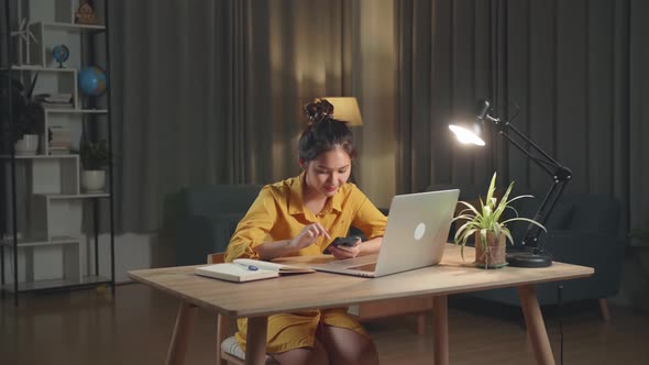 Asia Woman With Laptop Computer Calling On Smartphone From Home At Night