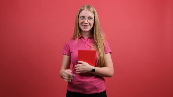 Positive Girl Sitting with a Notebook in Her Hand and Straightening Her Glasses