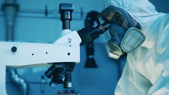 A Man in a Hazmat Suit is Using a Microscope for Analysis