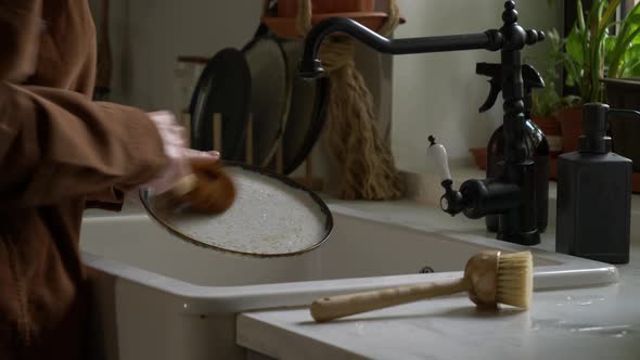 woman washes a plate in the kitchen using eco-friendly brushes