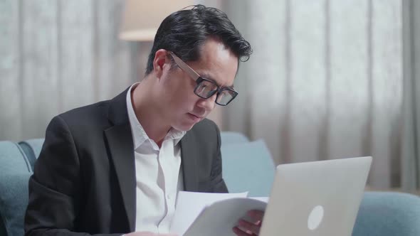 Close Up Of Asian Businessman In Jacket And Shorts Checking The Documents While Working A Laptop