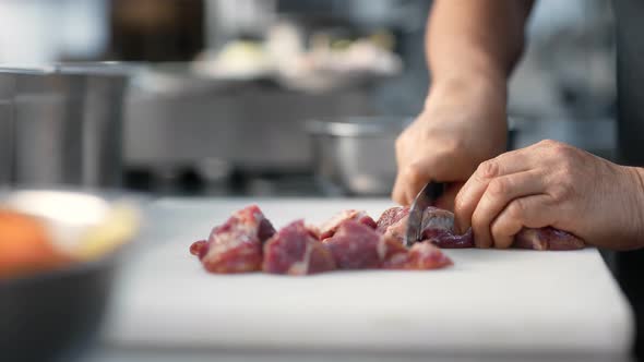 Mature Male Chef Hands Chopping Beef on Board Using Knife Closeup