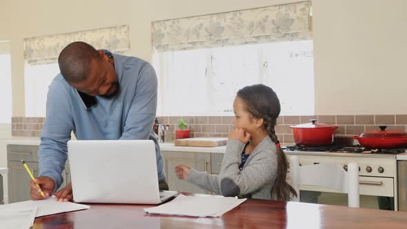 Father talking on mobile phone while daughter sitting beside in kitchen 4k