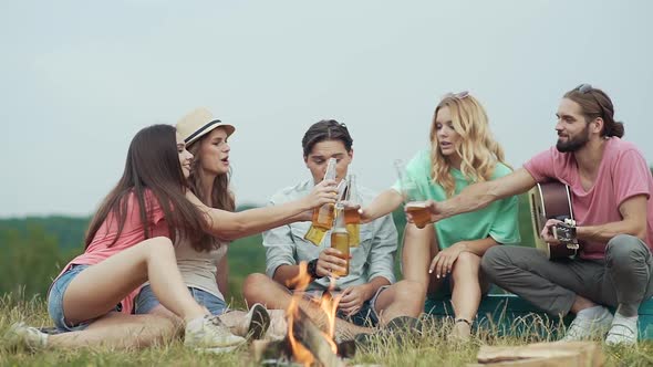 Happy Friends Drinking Beer, Having Fun And Sitting Near Bonfire