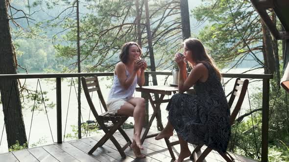 Two Attractive Girls Are Sitting at a Coffee Table on the Balcony, Enjoying Nature. Two Girlfriends