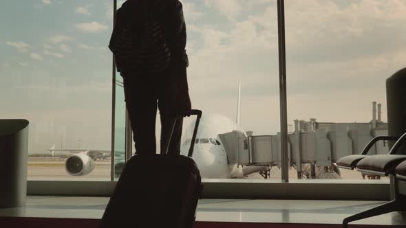 A Woman with Luggage Goes To a Large Window in the Airport Terminal