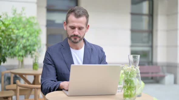 Man Working on Laptop Sitting in Outdoor Cafe