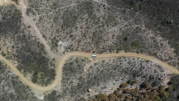 White car driving down dirt road, descending aerial from above