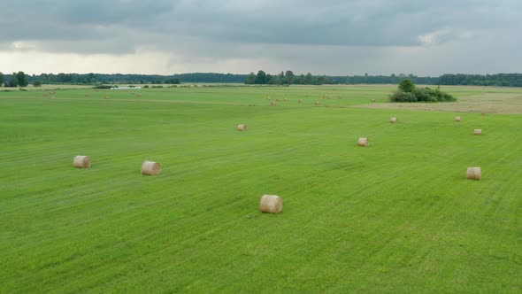 Scenic landscape flight above several hay rolls in green grassy farmland towards majestic hills and