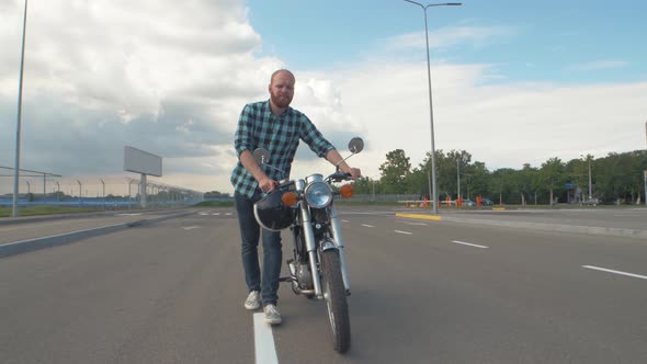 A Male Motorcyclist Rolls His Broken Motorcycle Along the Street