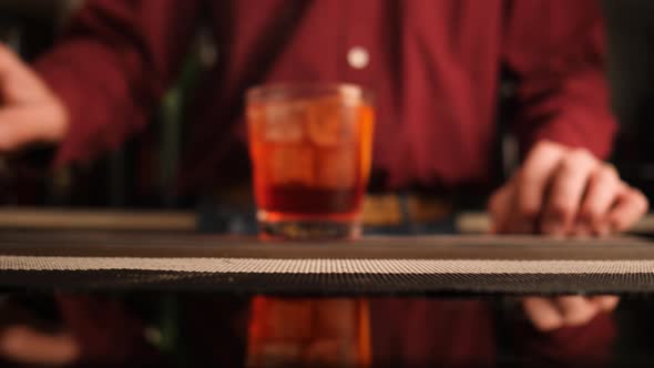 Bartender serves a Negroni cocktail on the bar counter. Slow Motion.