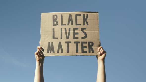 Black Lives Matter poster against blue sky. Woman hands hold poster Black Lives Matter. 