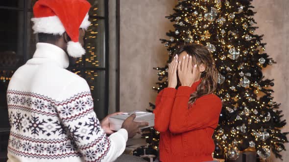 Disgruntled African Amerin Woman in a Red Sweater Throws New Years Gift in a Box with a Garland