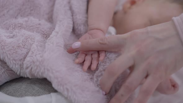 Closeup Female Caucasian Finger Touching Little Palm of Baby Girl Sleeping at Background