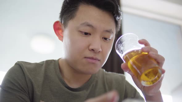 A Young Asian Man Works on a Smartphone and Drinks Beer  Closeup From Below