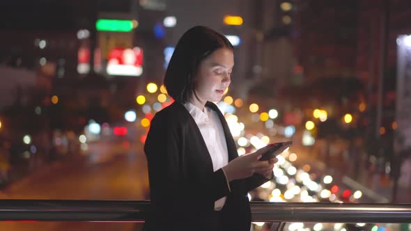 Asian young business woman standing outdoor chatting on mobile phone downtown in city at night.