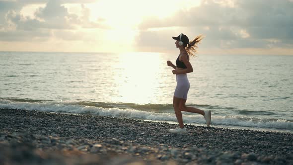 A Young Woman Runner is Listening to Music in Earphones and Training By a Sea