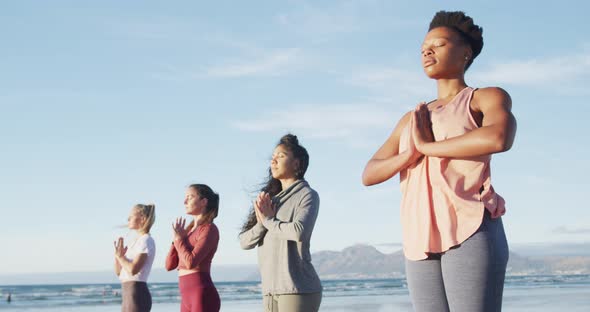 Group of diverse female friends practicing yoga at the beach
