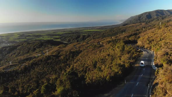 Camper Van Traveling a Mountain Road Towards the Ocean in New Zealand (Aerial Drone Shot)