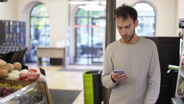 Relaxed Man Walking Through the Store Looking at the Screen of His Smartphone