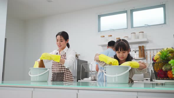 Asian young happy family teaching their little kid daughter to clean kitchen counter with happiness.