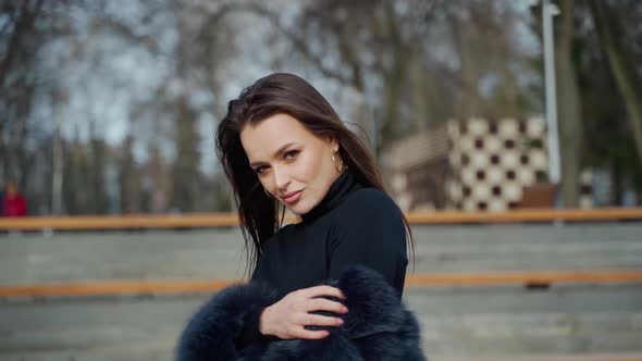 Portrait of beautiful model. Glamour girl in black fur coat posing on camera outdoors.