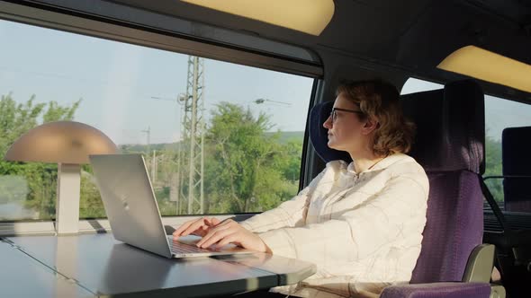 Woman Works on Laptop While Riding Train Sitting Near Window on Sunny Day