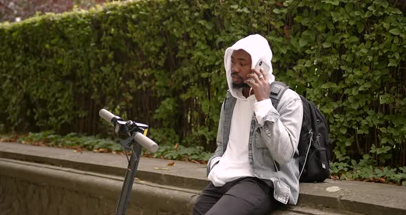 A Young Black Man Talking on the Phone Near an Electric Scooter