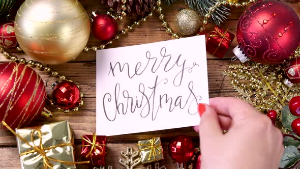 Woman's hand putting a card with the text MERRY CHRISTMAS on a wooden table