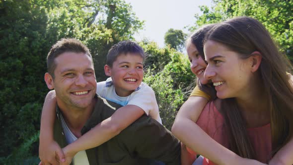 Portrait of caucasian couple carrying son and daughter on their back in the garden