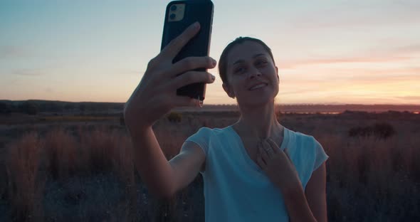 Front View of Beautiful Brunette Woman Making Selfie on Colorful Sunset