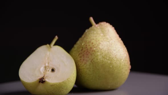 A whole pear and half a pear are lying next to each other. Ripe juicy yellow fruits with water drops