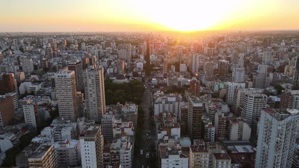 Dolly in flying over Belgrano neighborhood tall buildings at sunset with shiny sun in background, Bu