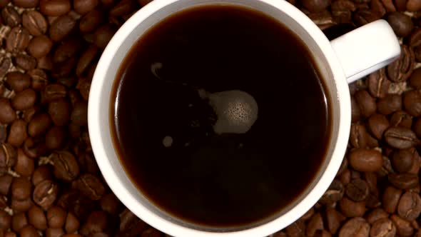 White Cup with Coffee Stands on Brown Beans, Sacking, Close Up