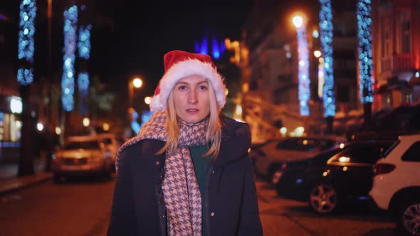 A beautiful woman in a Santa Claus hat walks at night on Christmas