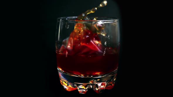 Falling ice cubes into a whiskey glass on an isolated black background. Slow motion.