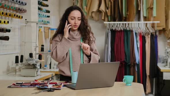 Successful tailor entrepreneur is talking on mobile phone and using laptop. Woman is busy